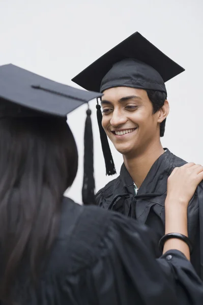 Man in graduation gown looking at a woman