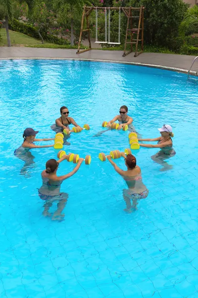 Smiling group doing aqua aerobics in swimming pool with dumbbells