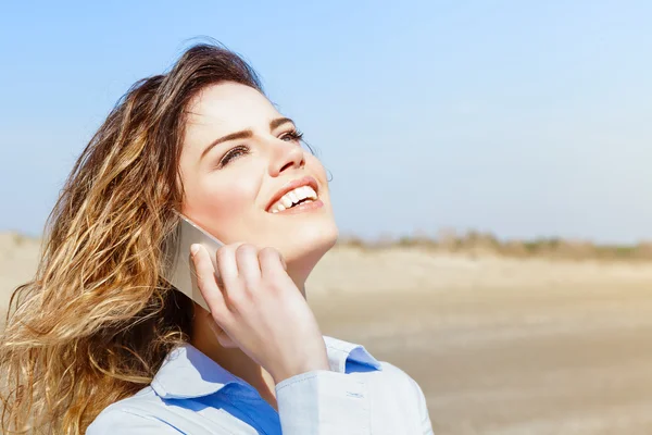 Happy woman laughing on the mobile phone on the beach