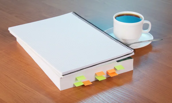 The book with bookmarks, a exercise book a cup of coffee with a saucer and a spoon, on a table