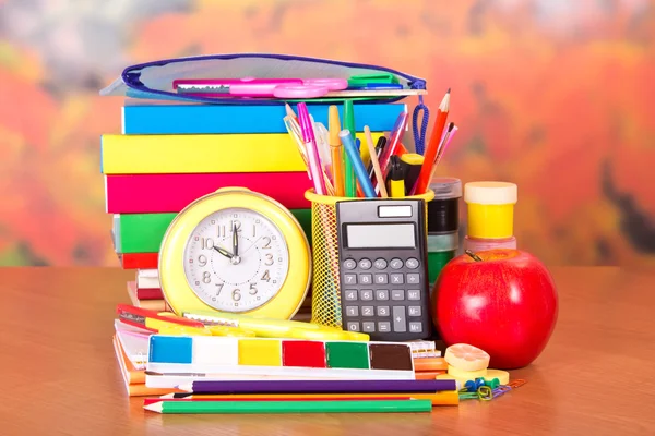 Books, alarm clock, pencil-case, a set of school accessories and an apple, on a table