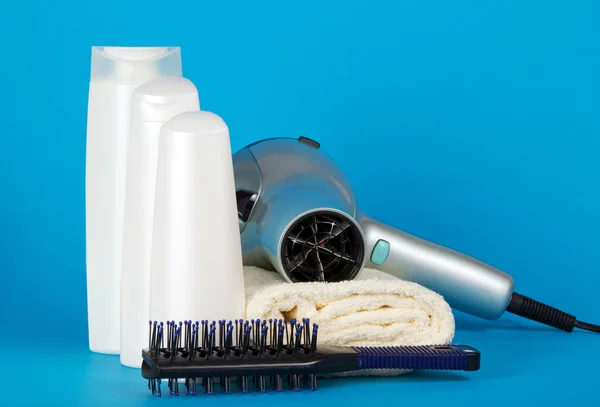 Set of cosmetics, the hair dryer and hairbrush on a towel on a blue background