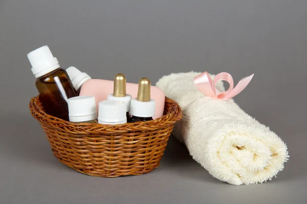 Hotel cosmetics kit and terry towel in basket, on a grey background