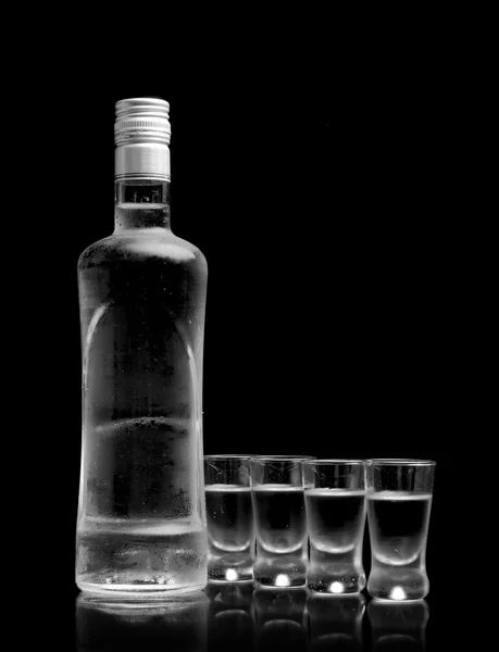 Bottle with many glasses of vodka isolated on black background