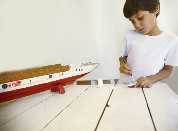 Boy painting and renovating old wooden boat