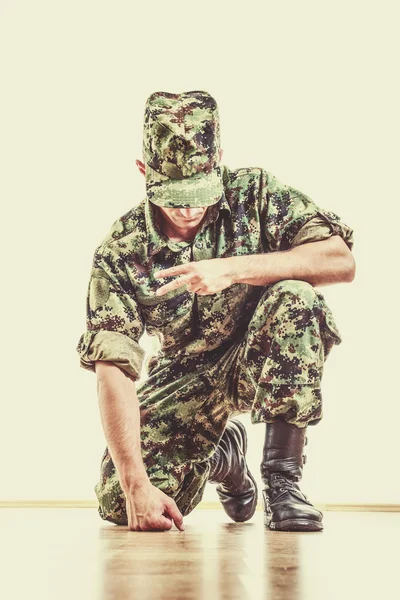Soldier with hidden face in green camouflage uniform and hat kne