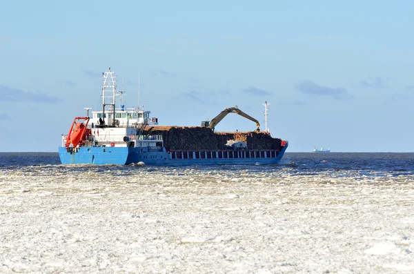 Cargo ship loaded with trees sailing in sea full of ice in winte