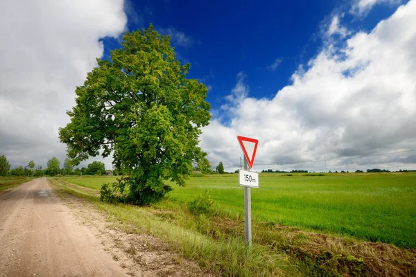 Green field and the road sign on a country road against stormy sky