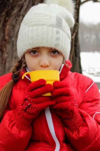 Girl holding a cup of tea at a picnic in winter gloves