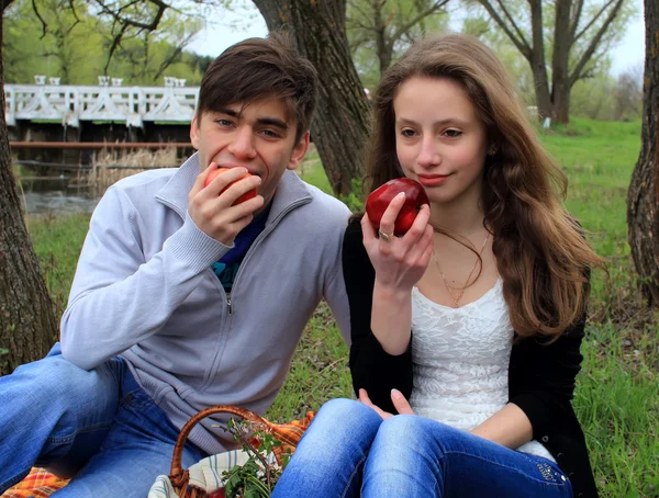 Young man and woman eat apples on a picnic in the park