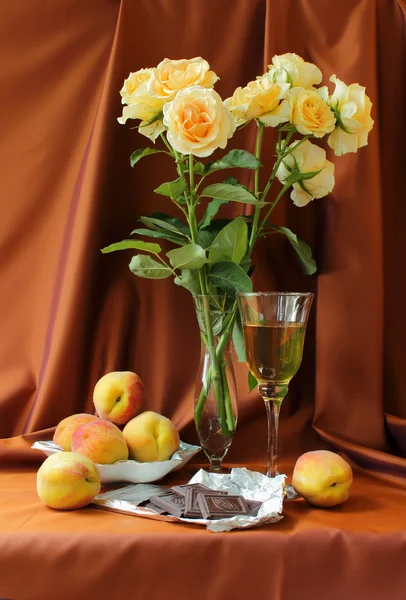 Still life with roses and glass of wine, peaches and chocolate