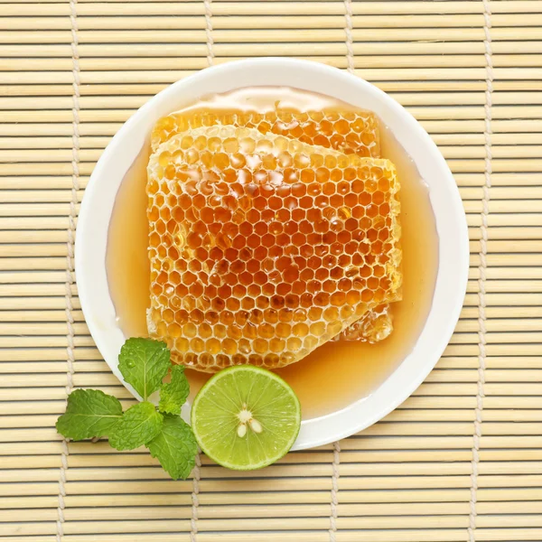 Sweet honeycombs in dish with lemon and mint on bamboo mat