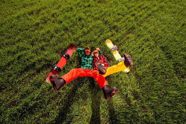 Couple in sportswear with snowboards lying on the grass