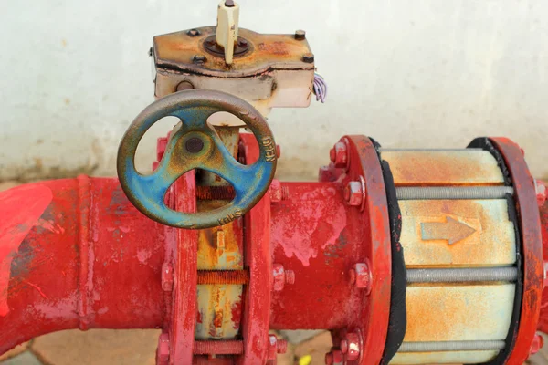 Red rusty metal industrial water pipes with a valve.