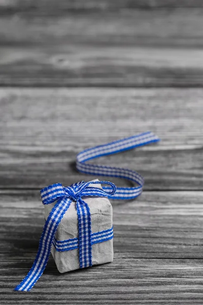 Gift box with blue checked ribbon on wooden grey background.