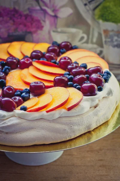 Pavlova with whipped cream, peaches, cherries and plums