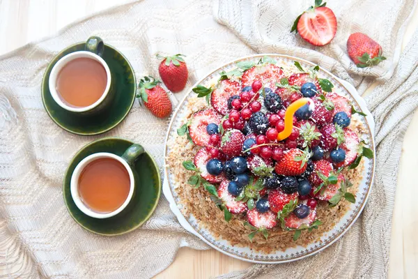 Napoleon cake, decorated with fresh berries, strawberries, blueberries and blackberries, with birthday candle. Two green tea cups and teapot near the window.