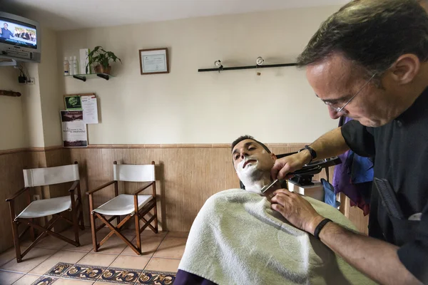 Barber shaving with a razor to young man