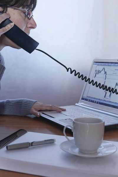 Close-up of female calling by phone in front of a laptop with a coffee in the office