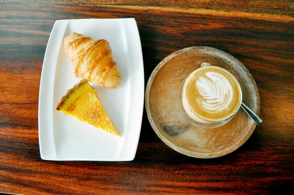 A cup of Hot Coffee, Croissant and Passion fruit Tart on wood ta
