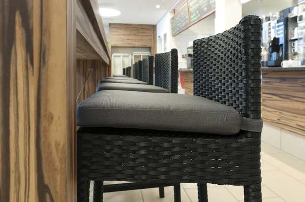 Aligned high rattan chairs with seat-contact surface in front of wooden table in self service restaurant