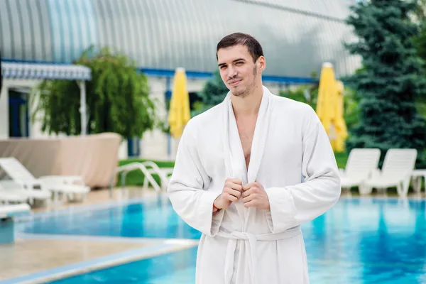 Man in a bathrobe stands near the pool