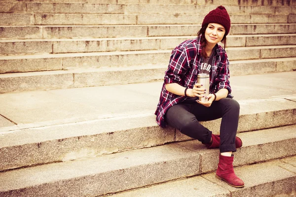 Brunette woman in hipster outfit sitting on steps on the street. Toned image. Copy Space