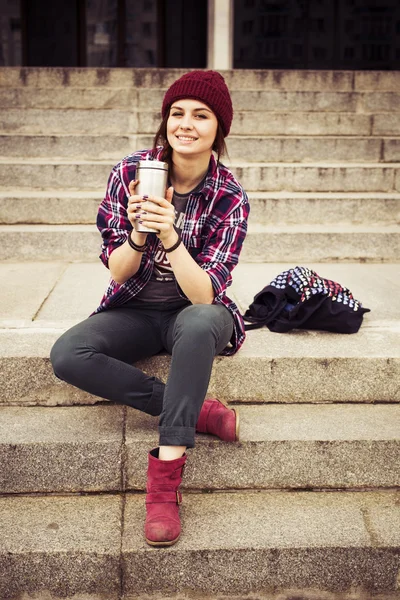 Brunette woman in hipster outfit sitting on steps on the street. Toned image