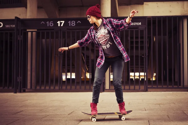 Brunette woman in hipster outfit skating on a scateboard on the street. Toned image. copy space