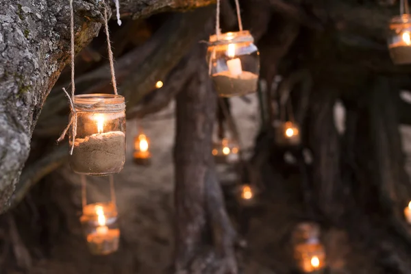 Beautiful decorated romantic place for a date with jars full of candles hunging on tree and standing on a sand. Copy Space