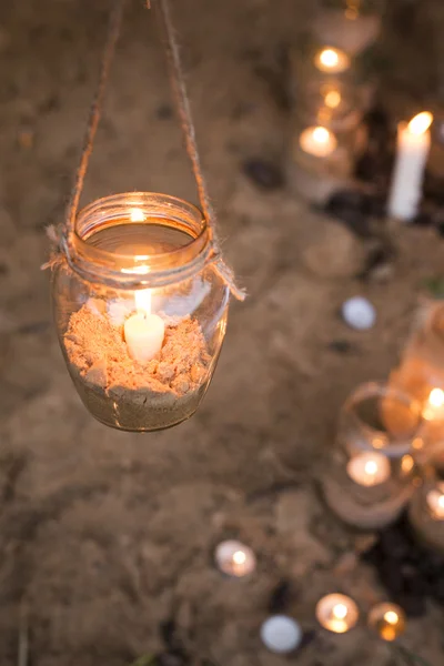 Beautiful decorated romantic place for a date with jars full of candles hunging on tree and standing on a sand