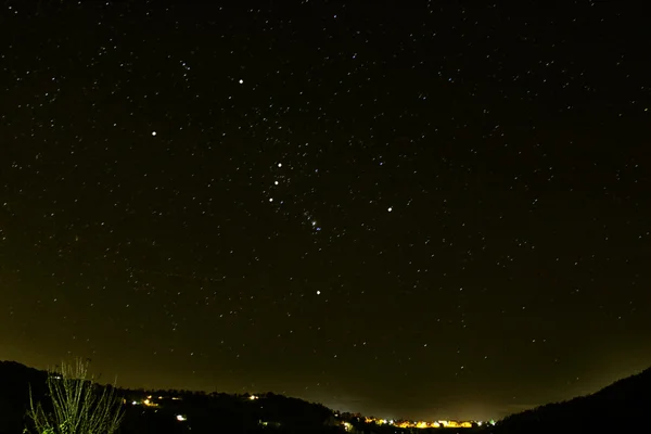 Orion constellation on the horizon over illuminated town