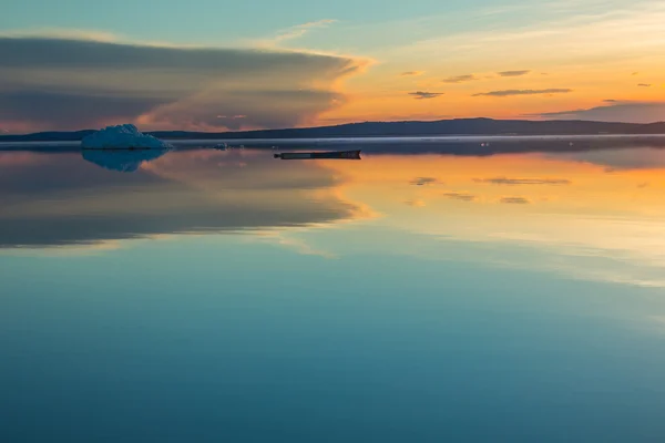 An old boat on the background of the melting iceberg on spring mountain lake in the setting sun.