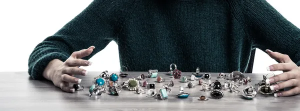 Closeup of young woman holding her hands around a table with many rings lying.