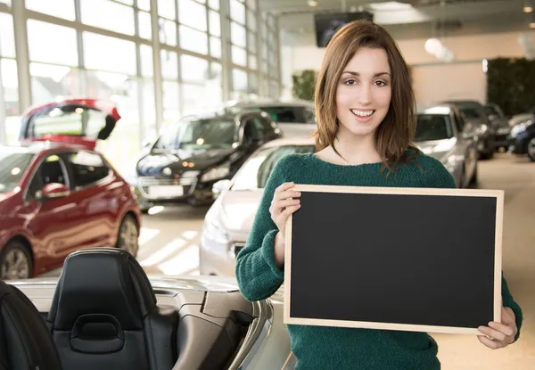 Young brunette holding blackboard inside car dealership