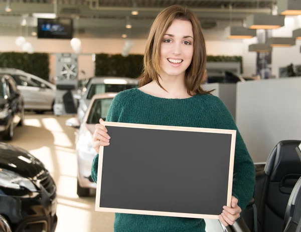 Young brunette holding blackboard inside car dealership