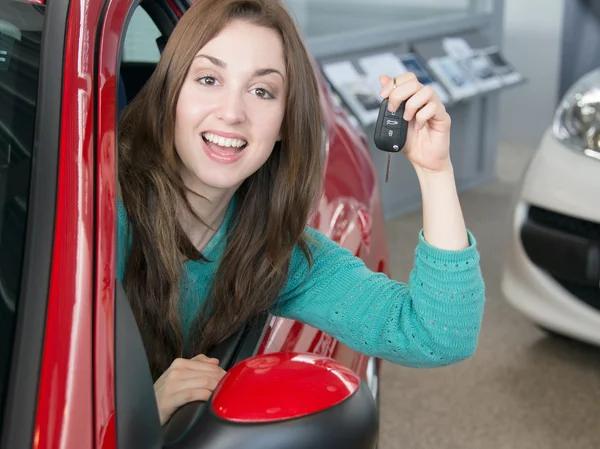 Young brunette holding car key inside car dealership