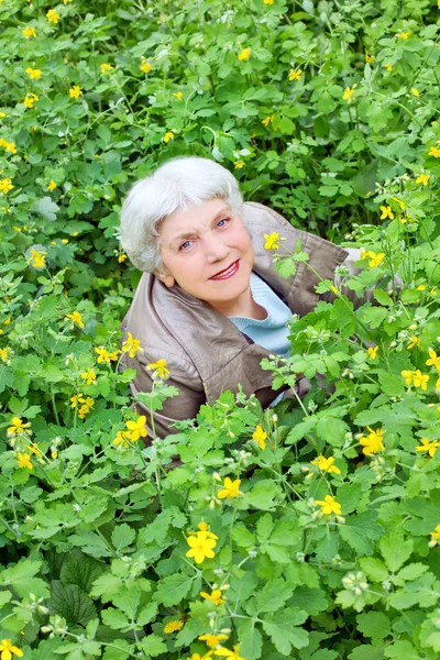 Happy beautiful elderly woman sitting on a glade of yellow flowe