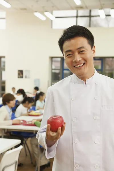 Chef in school cafeteria holding apple
