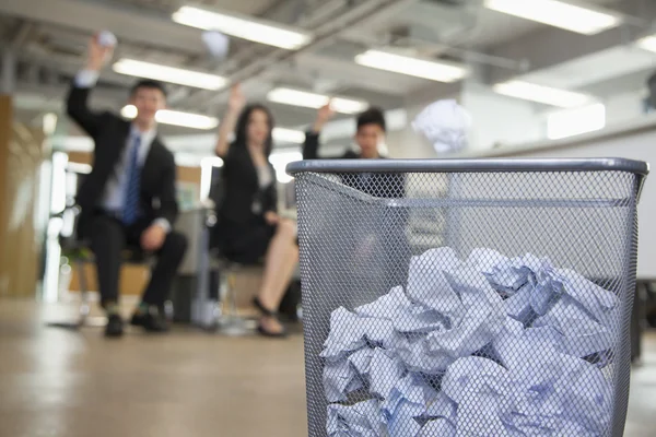 Coworkers preparing to throw paper into waste basket