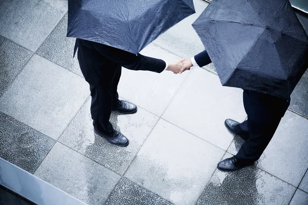 Businessmen shaking hands in the rain