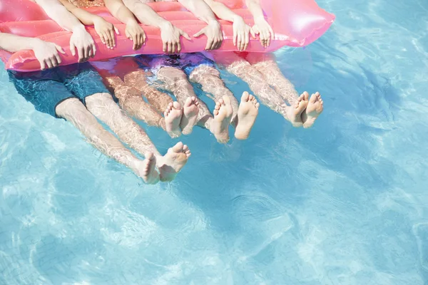 Friends in a pool holding onto an inflatable raft with feet sticking out of the water