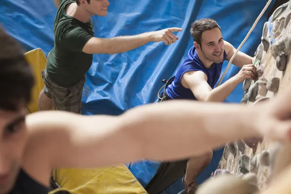 Men point and climbing in an indoor climbing gym