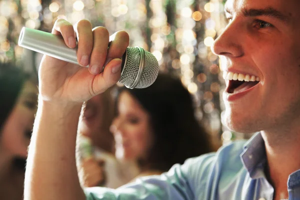 Man singing at karaoke, friends singing in the background