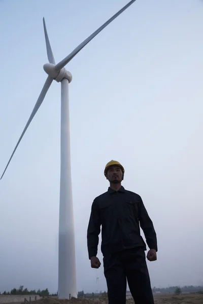 Engineer standing in front of a wind turbine at dusk