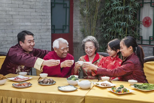 Family with cups raised toasting over a Chinese meal