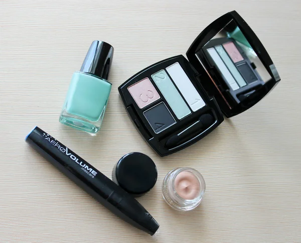 Set of eyeshadow, mascara, primer, turquoise blue nail polish on a dressing table