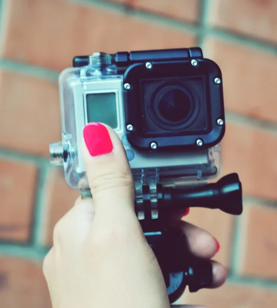 Hand with bright pink nails holding small camera in waterproof covering
