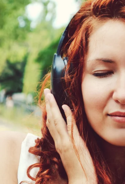 Beautiful redheaded woman in big headphones listening to the music with her eyes closed