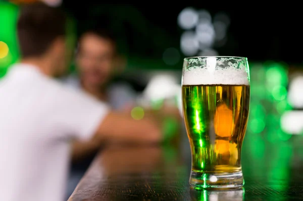 Glass with beer on bar with people talking on the background